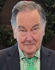 Elderly man in a suit and checkered shirt looking at the camera.